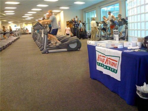 Krispy Kreme stand in large gym while people are working out on treadmills and stair steppers